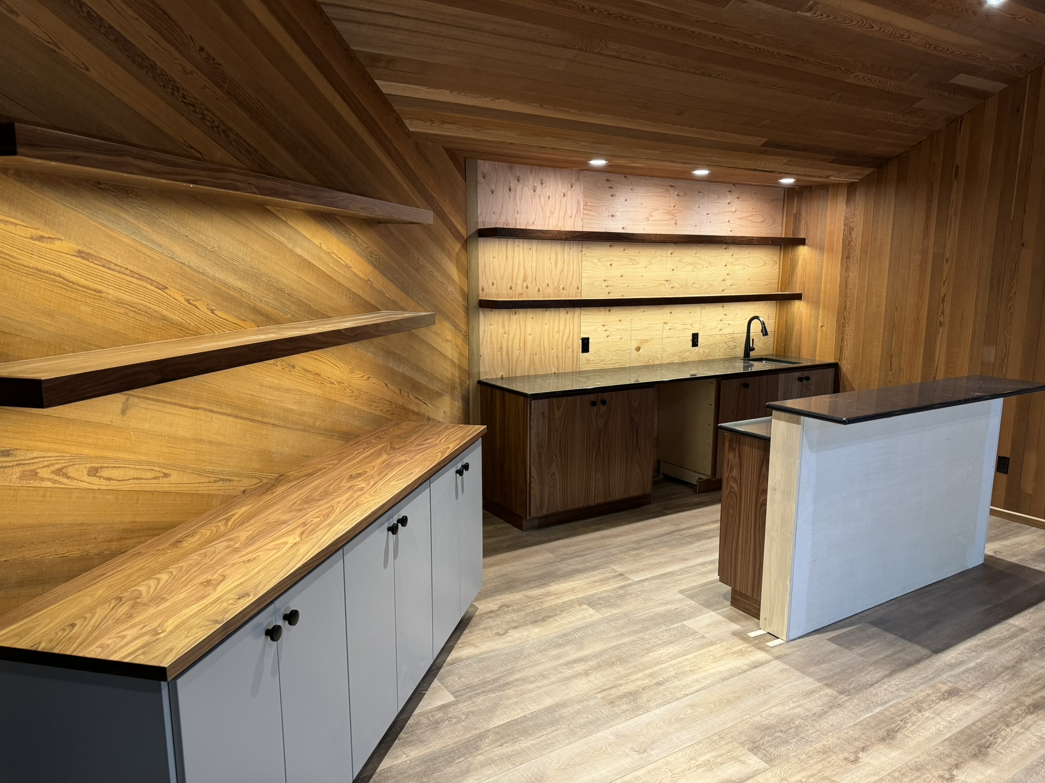 Custom wood-paneled wet bar with floating shelves, central island, and sink wall