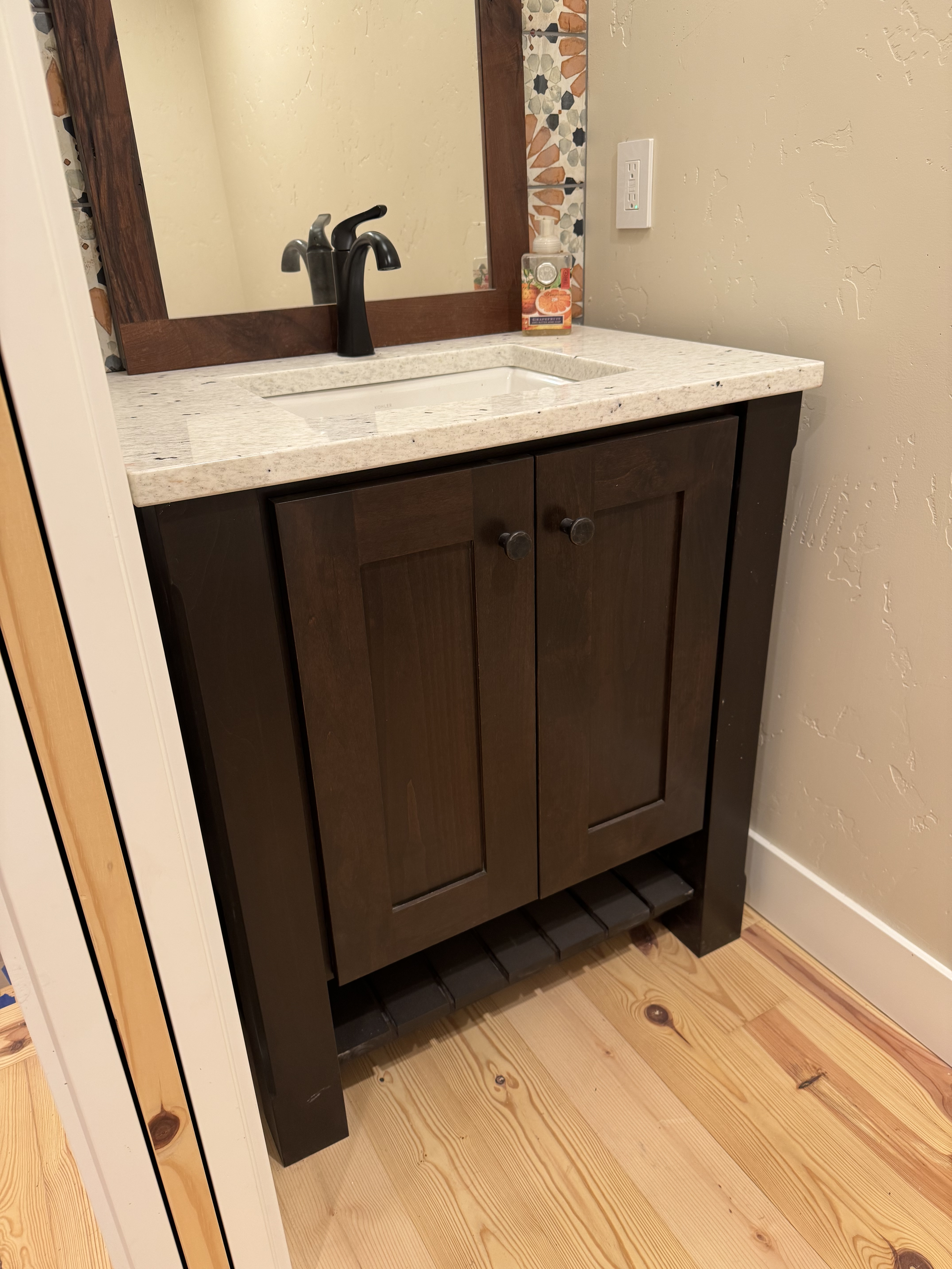 Dark espresso shaker vanity with three drawers installed in a bathroom with colorful tile backsplash and shiplap walls