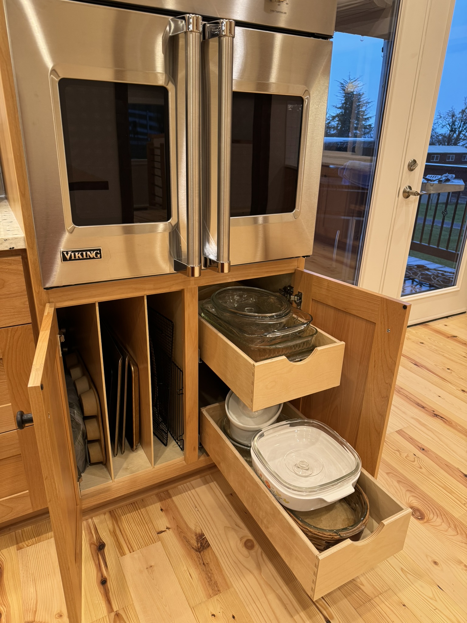Custom base cabinet below double wall ovens with pull-out drawers and tray dividers for organized cookware storage