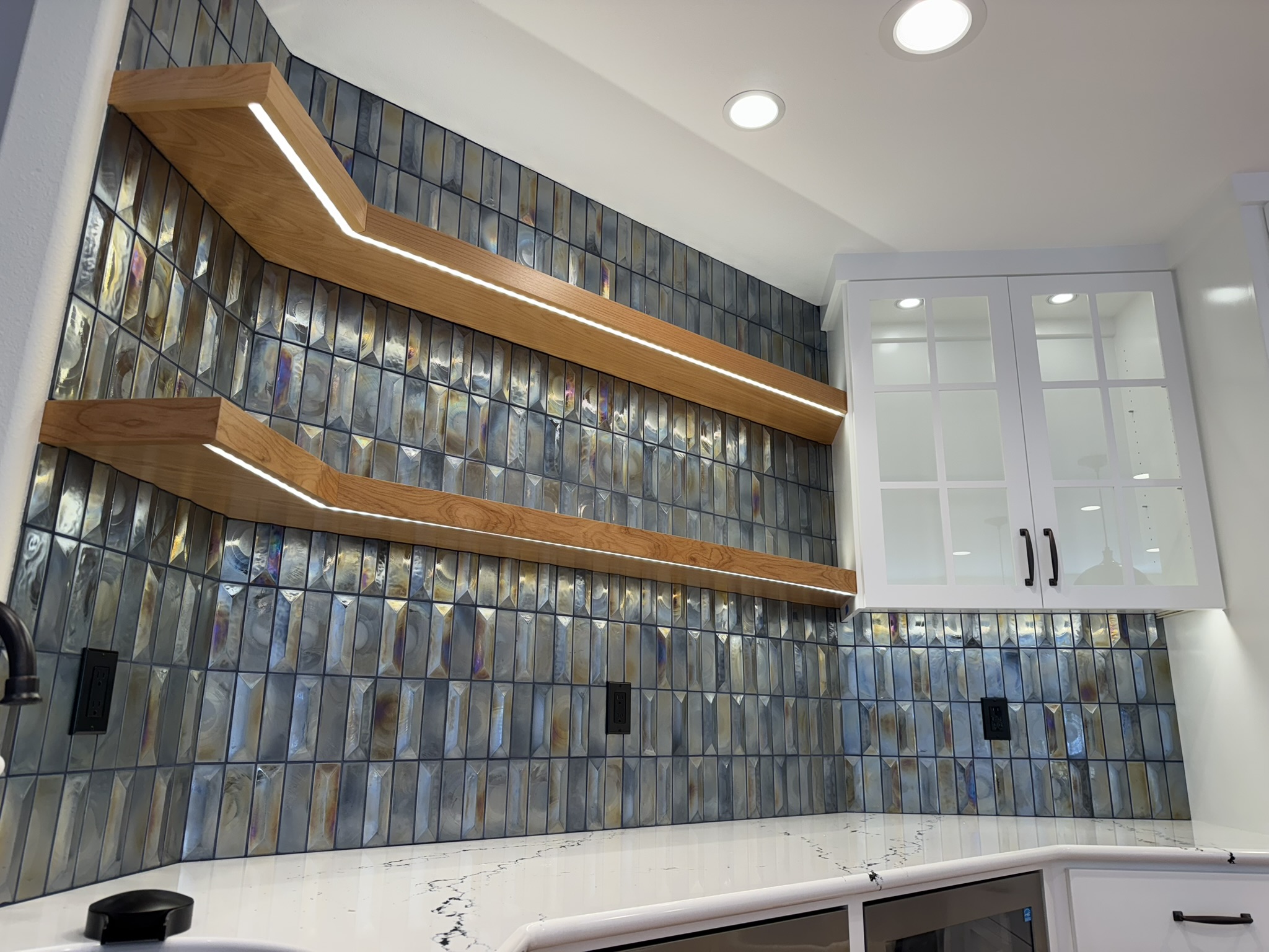 Iridescent tile kitchen with lit floating shelves over white cabinets
