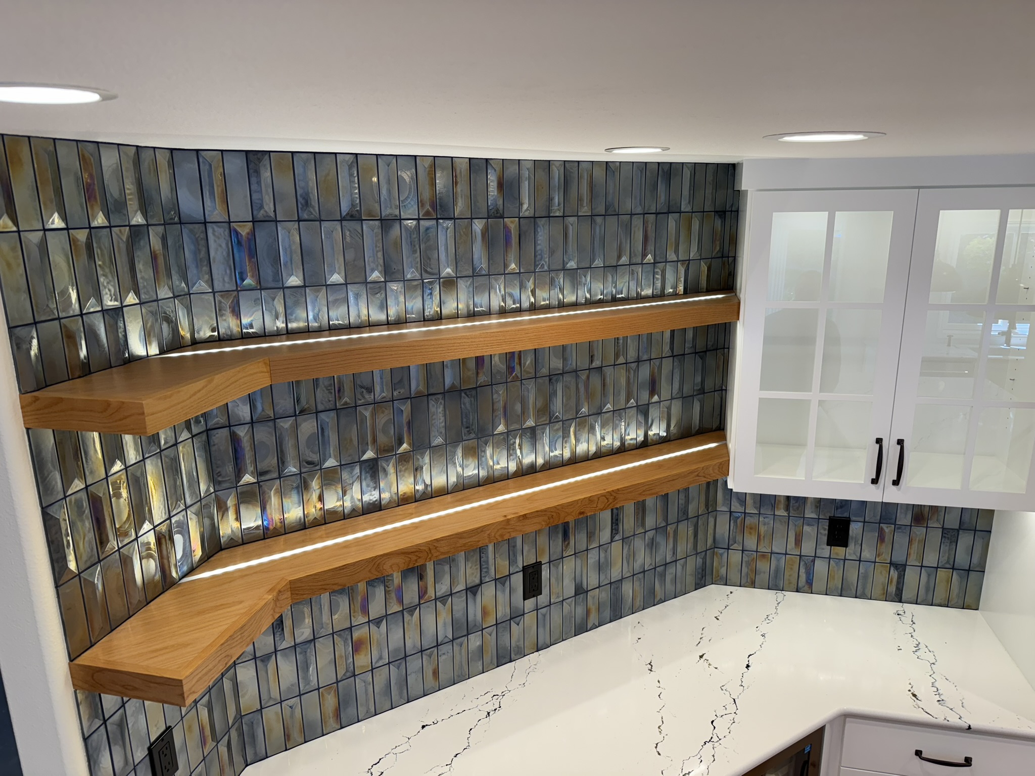 Detail of iridescent blue backsplash tiles and custom wood floating shelves with built-in lighting
