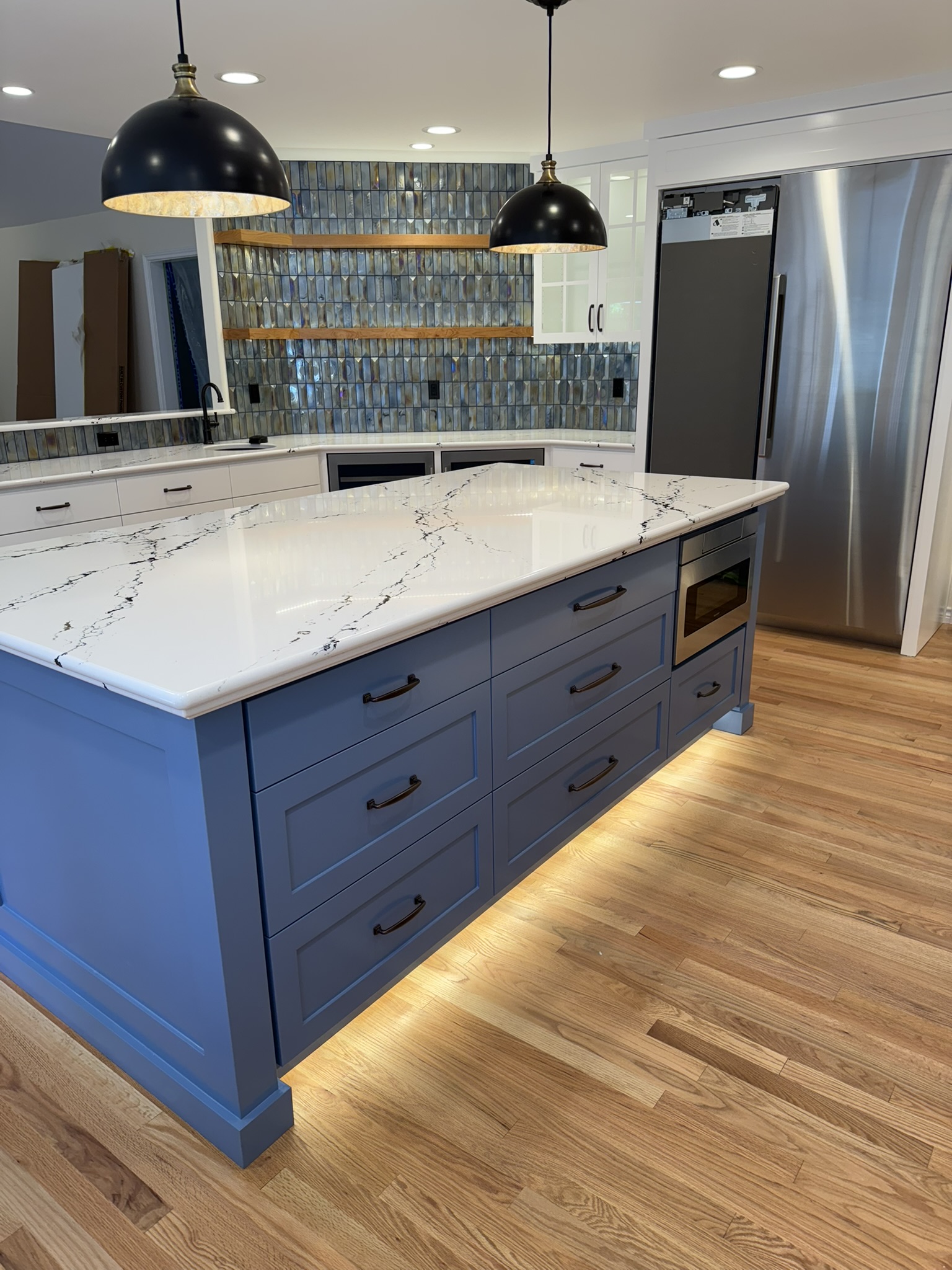 Wide kitchen view featuring a blue island with waterfall countertop and warm pendant lighting
