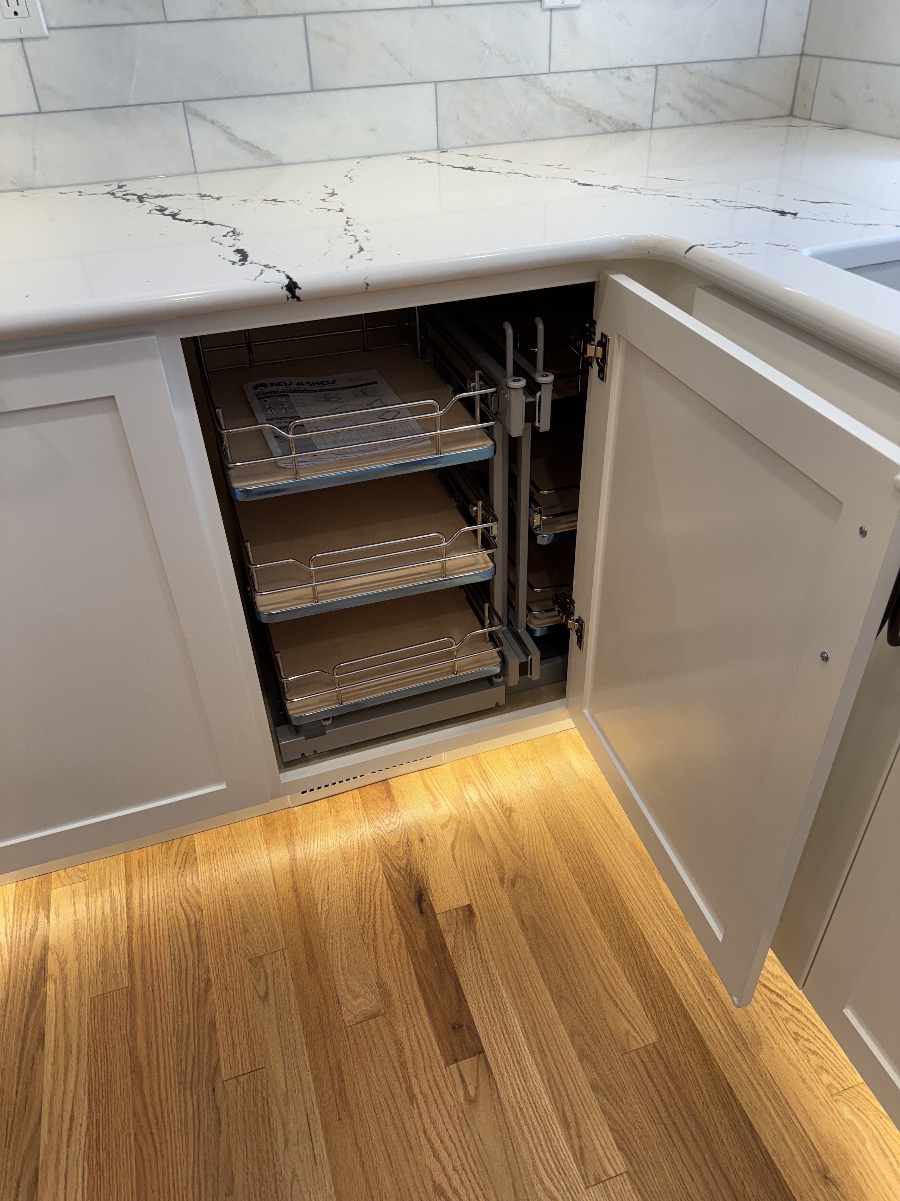Blind-corner pull-out organizer stored inside a white base cabinet with chrome rail baskets and pivoting slide hardware
