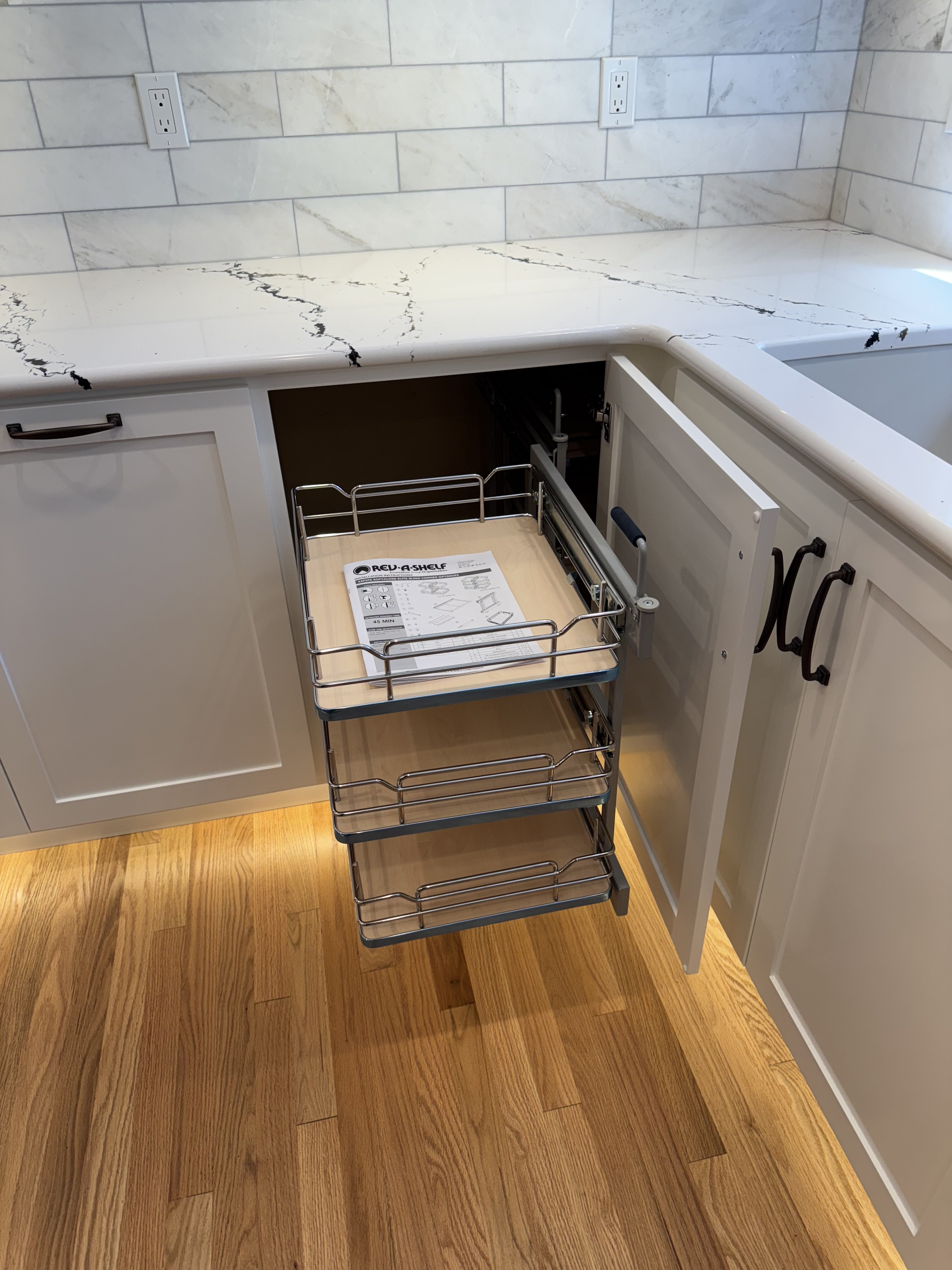Partially extended blind-corner organizer showing three chrome rail pull-out shelves sliding forward for access