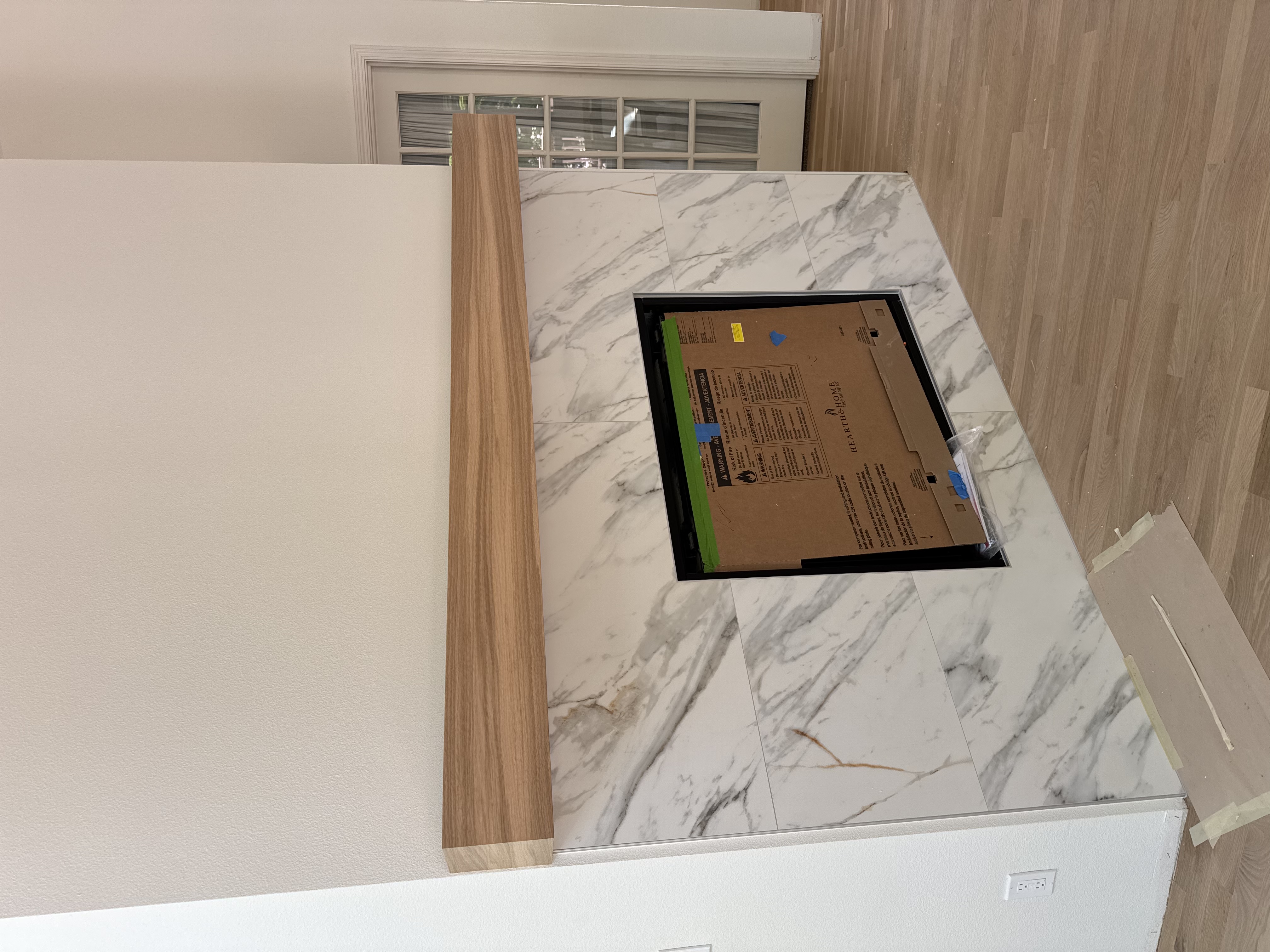 Custom island under construction showing marble-look stone countertop with inset cooktop opening and wood trim detail