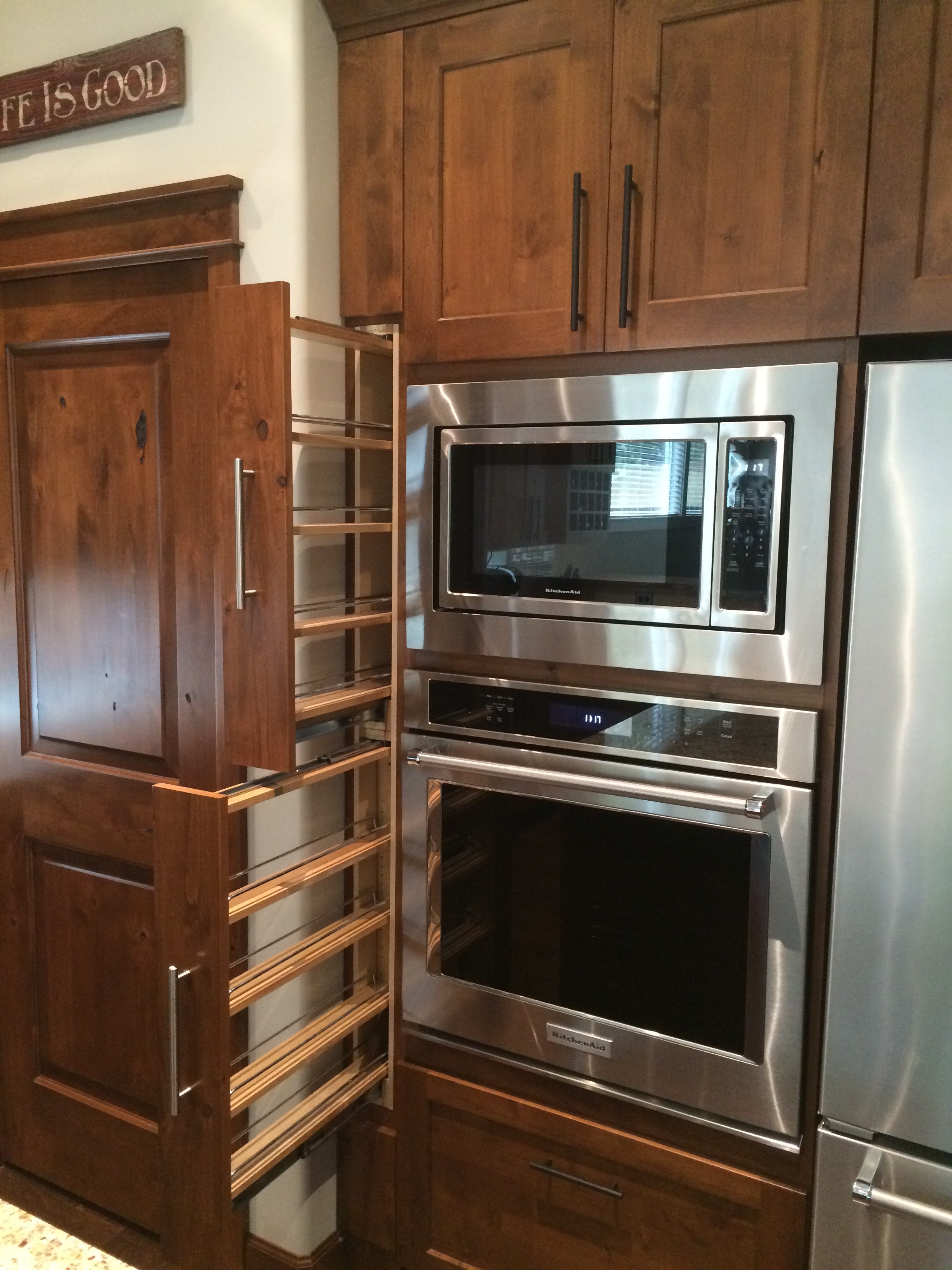 Custom tray-divider drawer pulled open below wall ovens, showing organized cookware storage