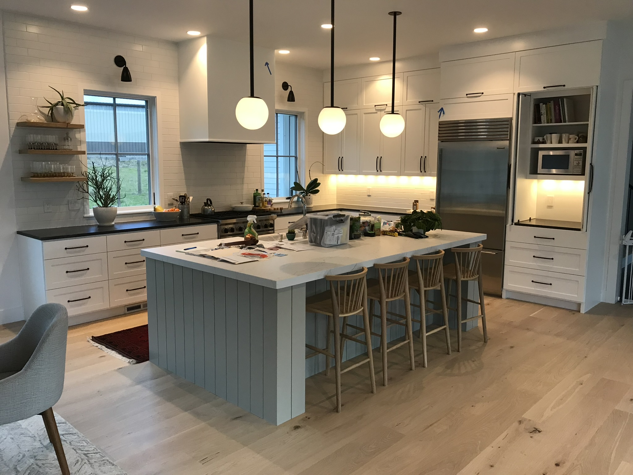 White farmhouse kitchen with painted dark island, open shelving, and stone backsplash