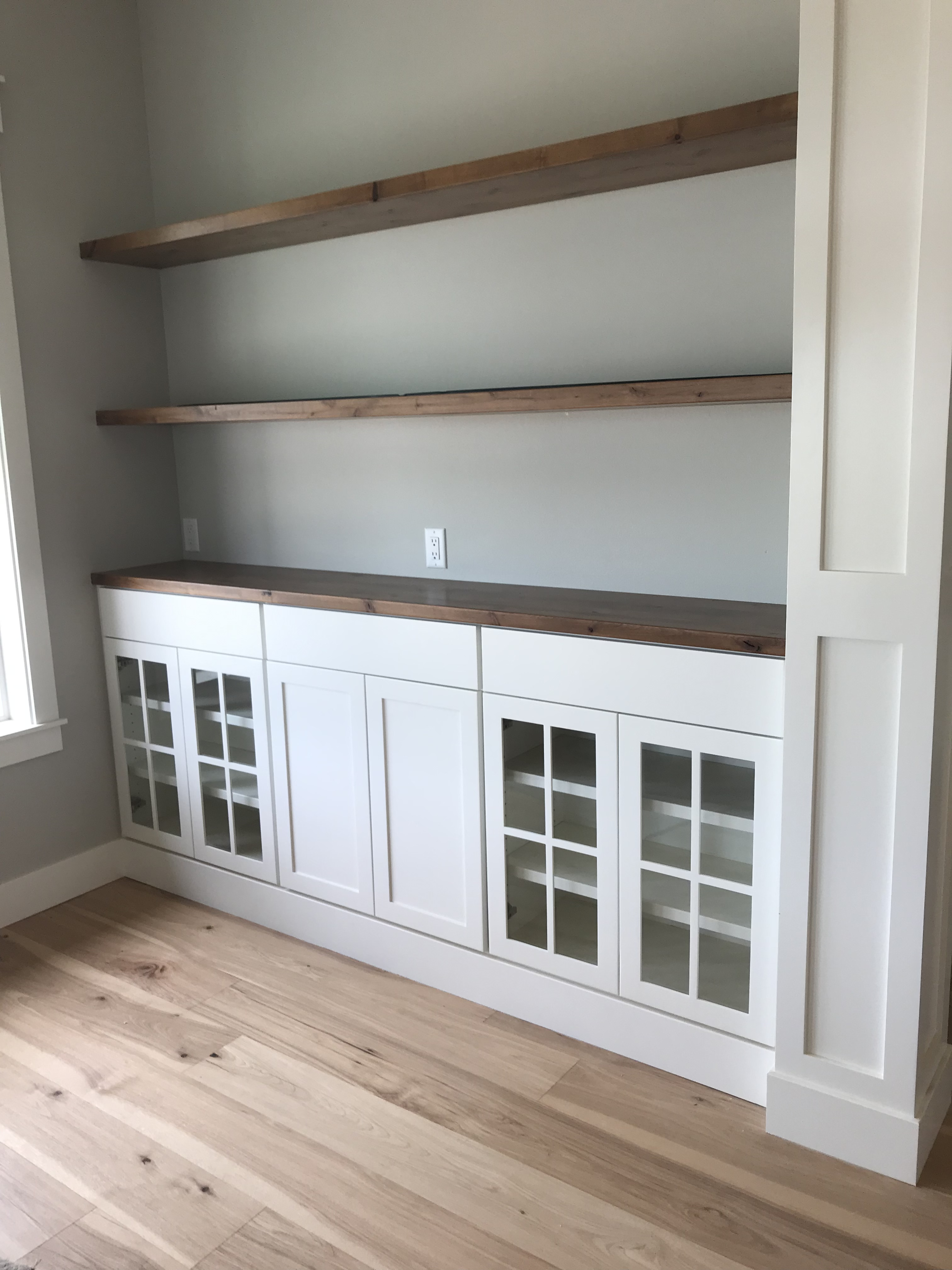 White glass-front built-in pantry cabinet with rustic wood beams framing the entry