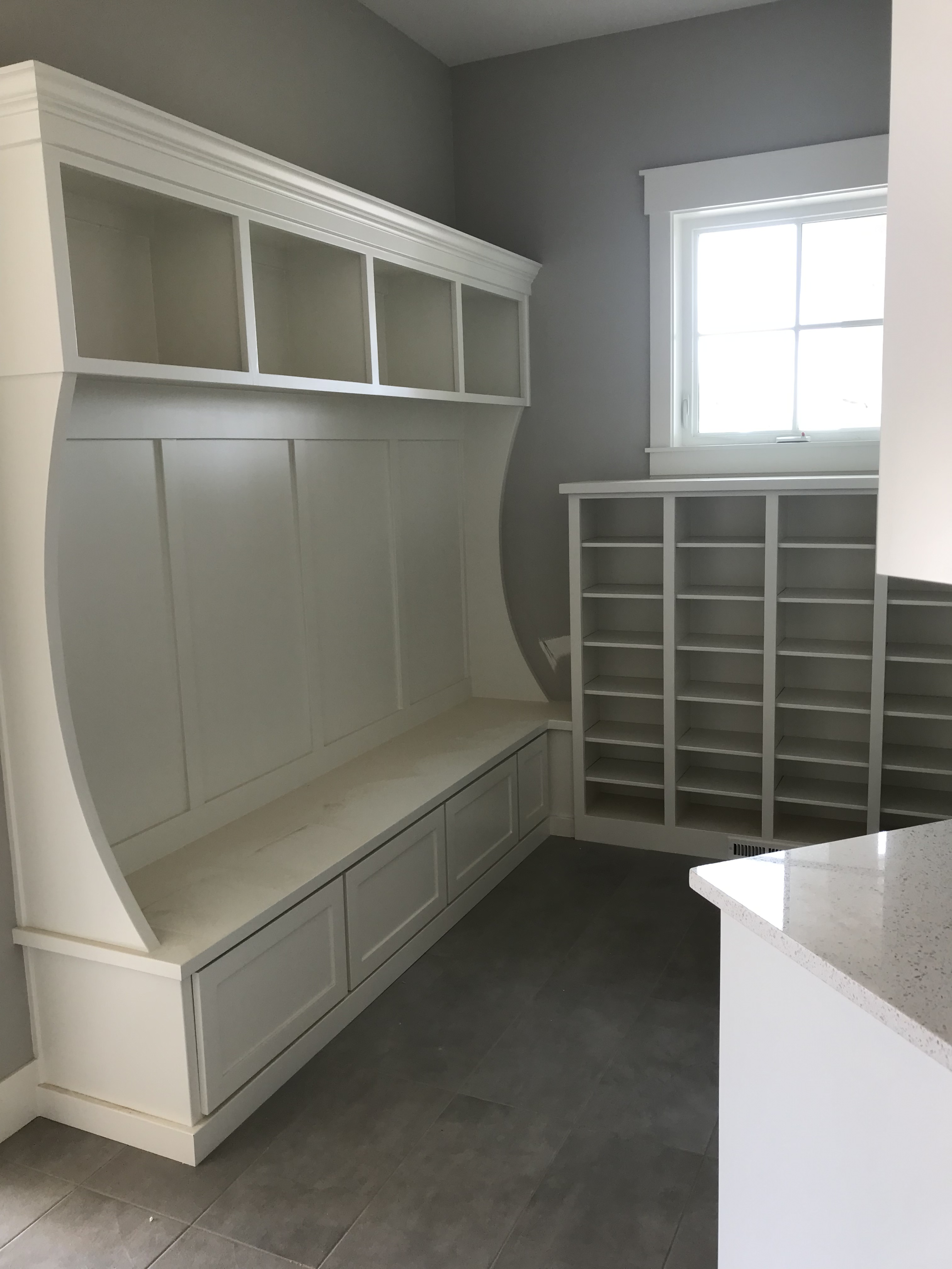 White painted mudroom with built-in bench seat, upper open cubbies, lower storage drawers, and full shoe cubby wall