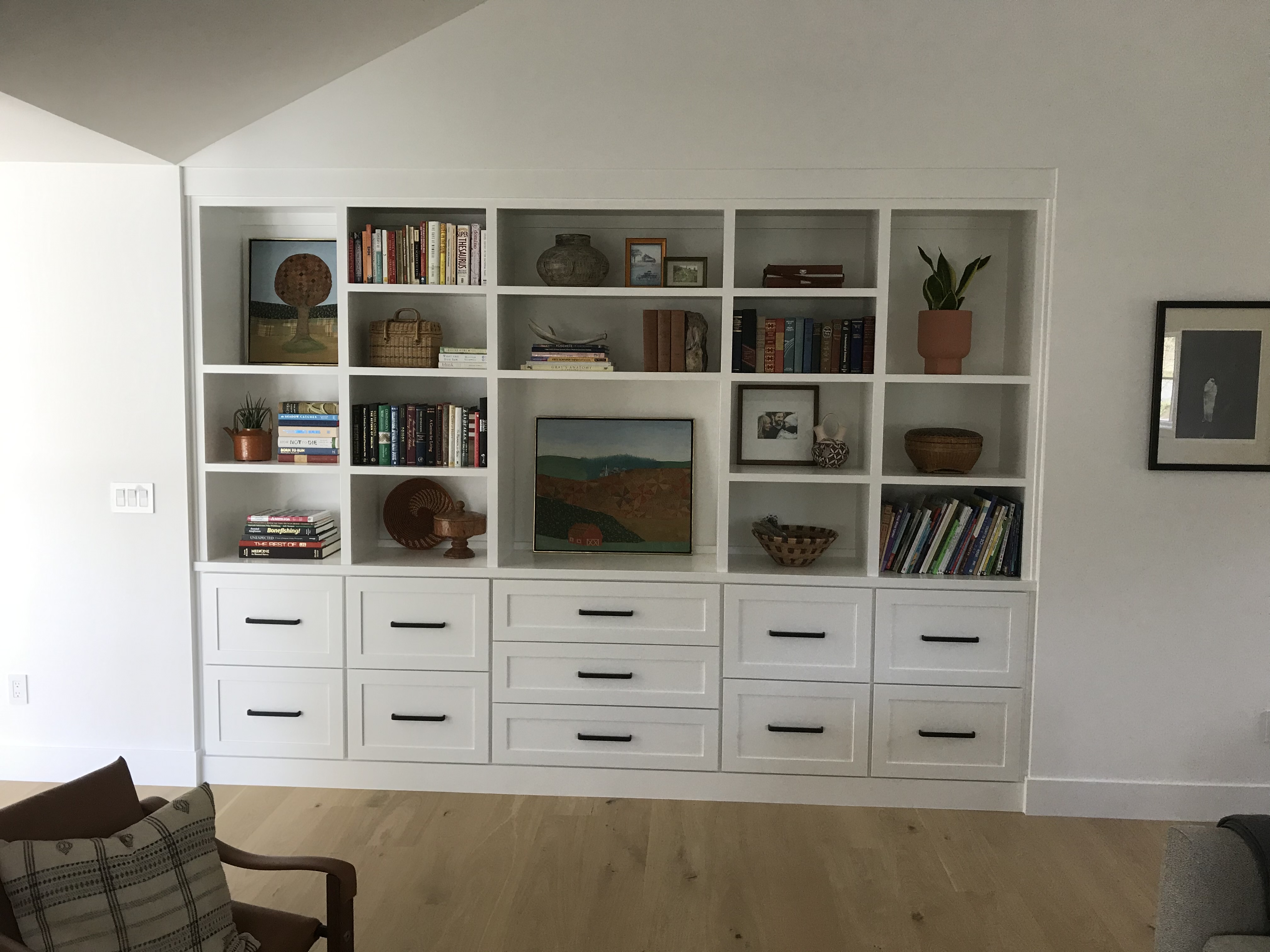 White wall-to-wall built-in with open shelving styled with books and decor above a full run of shaker base drawers