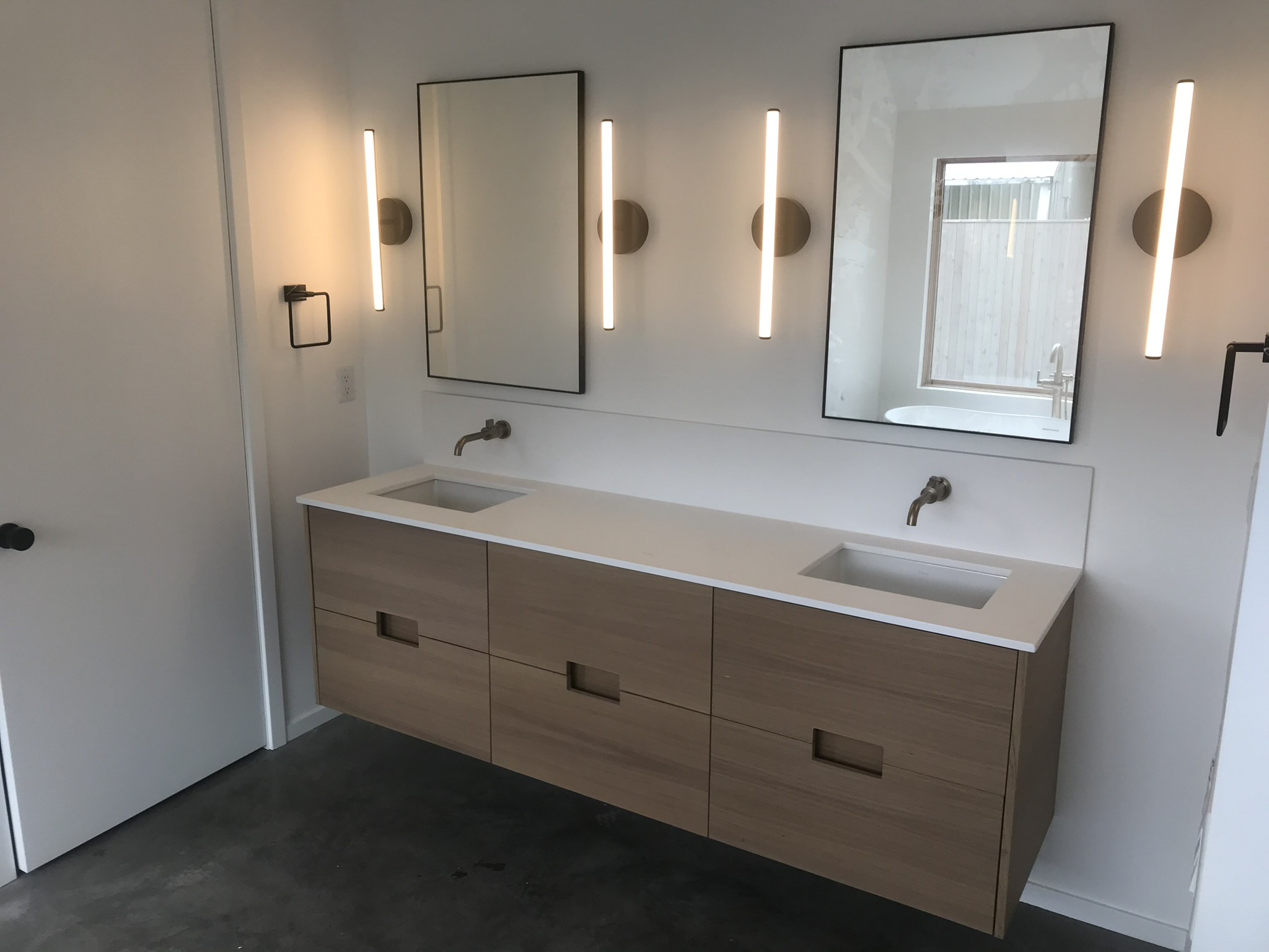 Wall-mounted double vanity with light wood drawer fronts, integrated sinks, and LED wall sconces