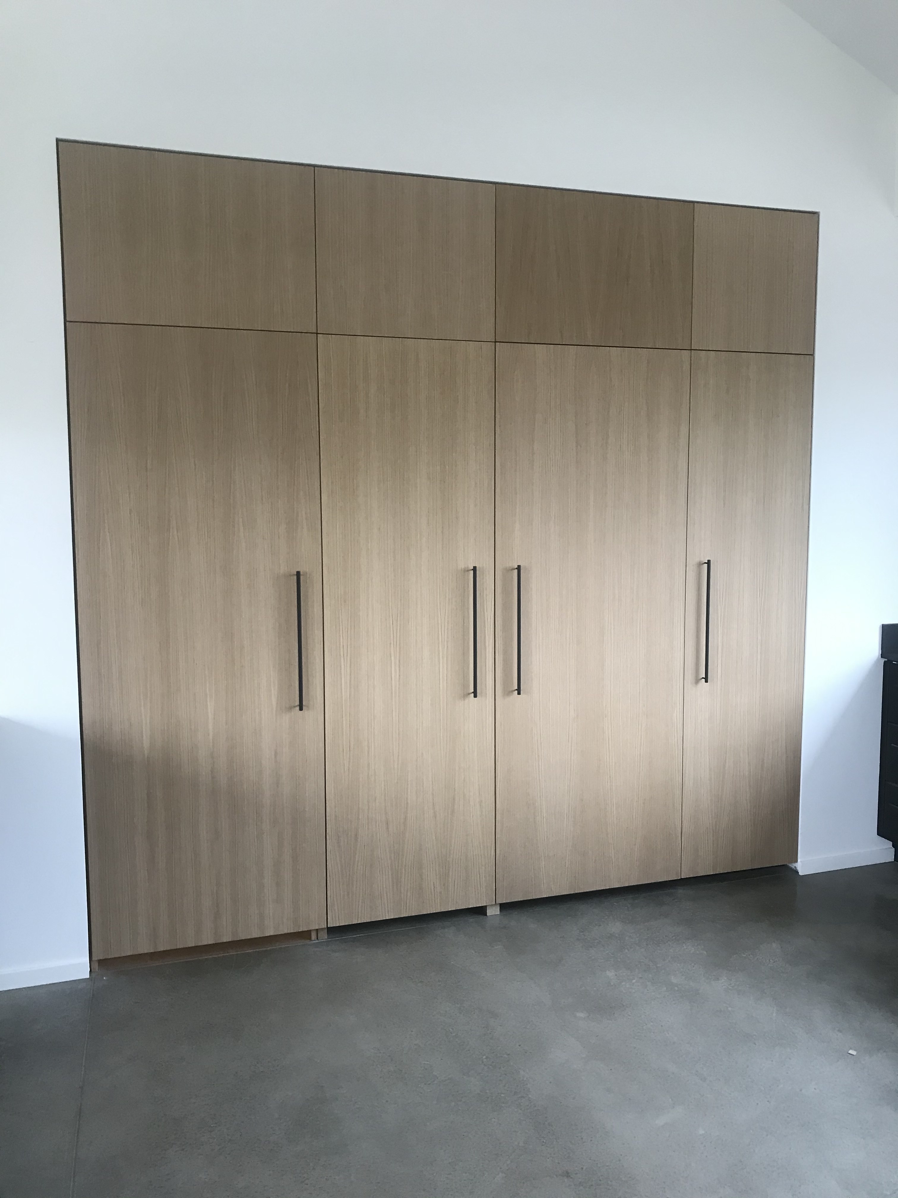 Modern flat-panel light wood wall with bar pulls — closed position, no indication a door is concealed within