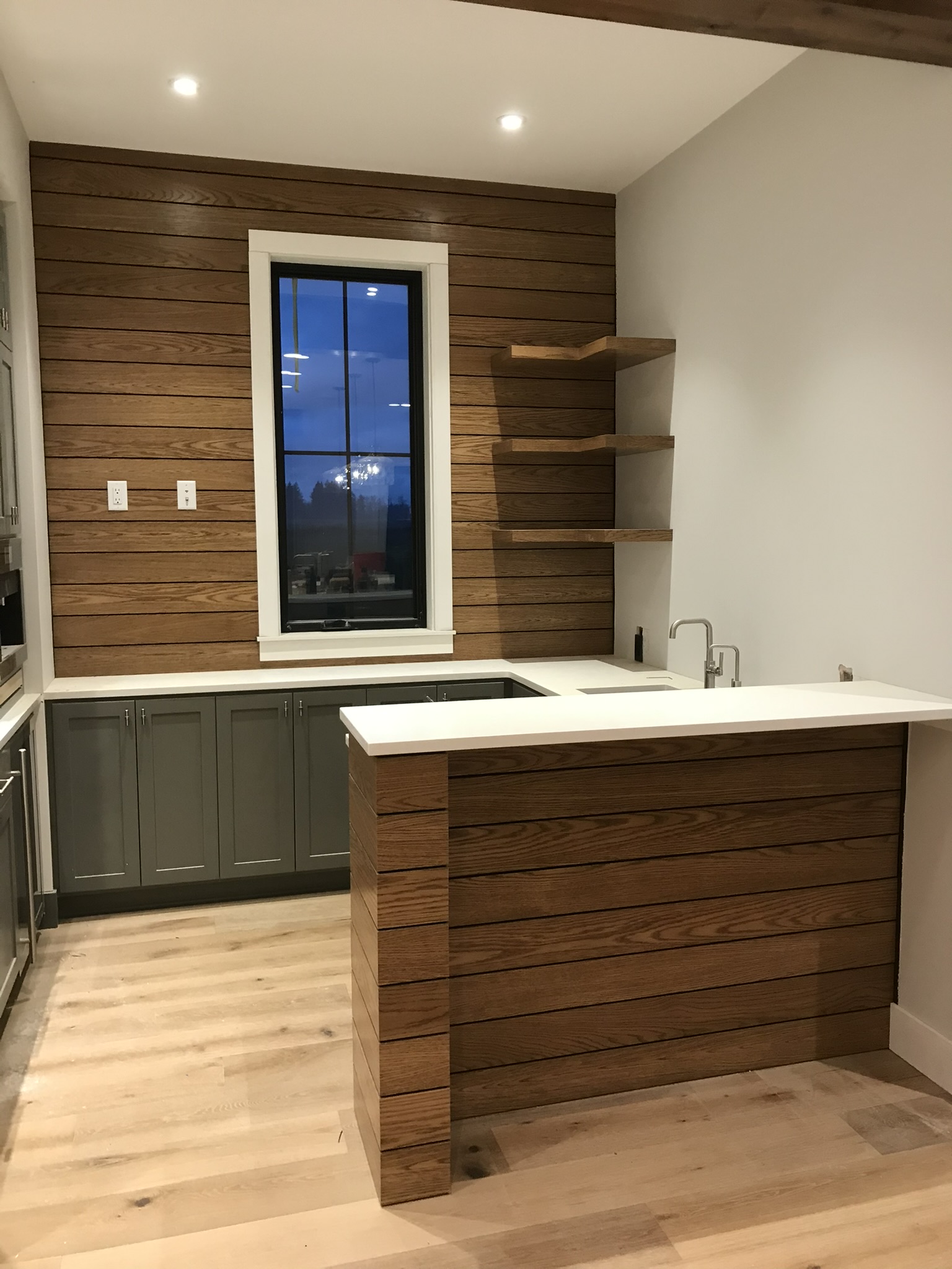 Straight-on view of wood-plank wet bar showing L-shaped countertop, floating shelves, and undermount sink