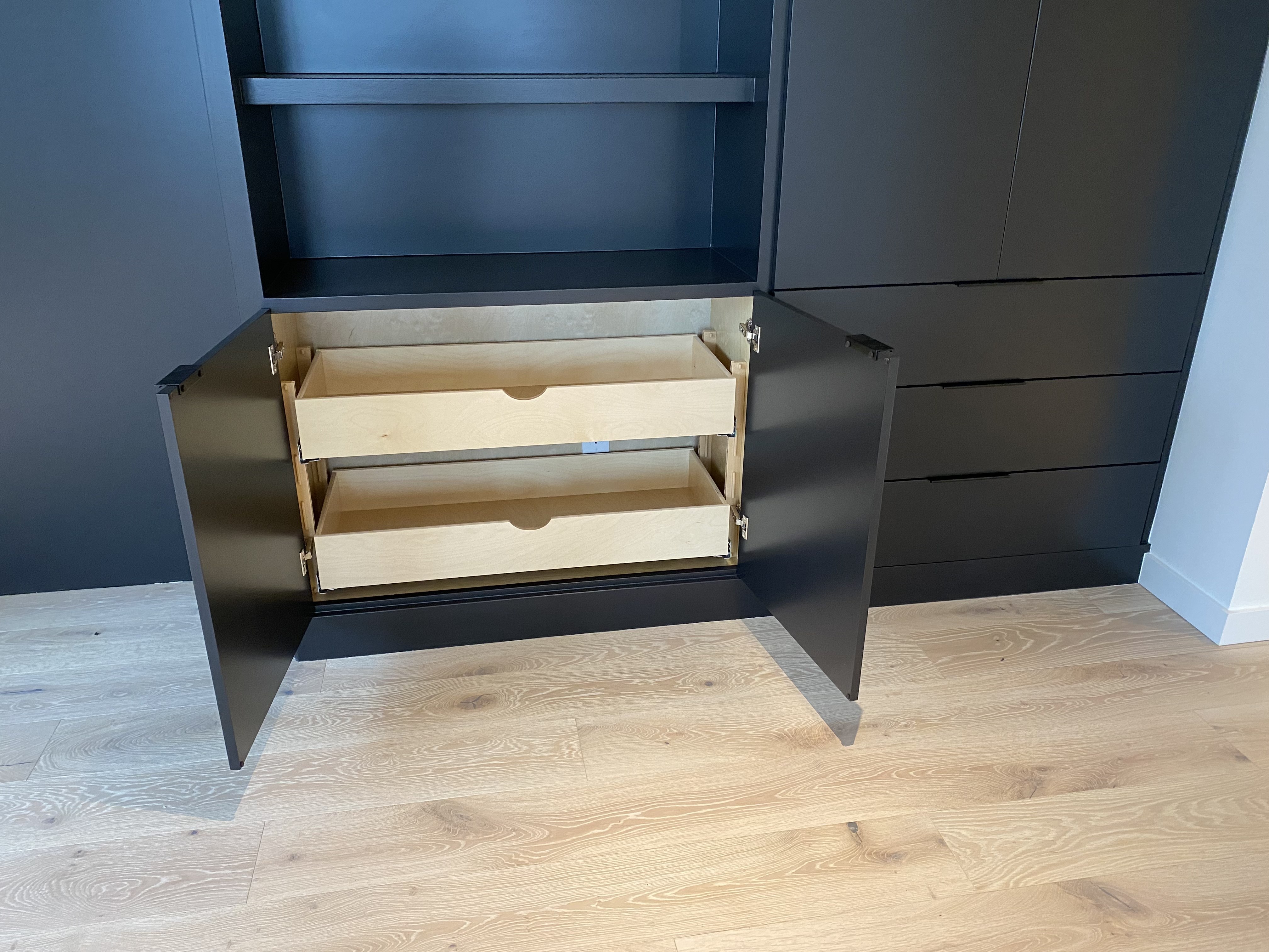 Interior detail of matte black built-in showing cabinet doors open with two pull-out drawers on Blum hardware