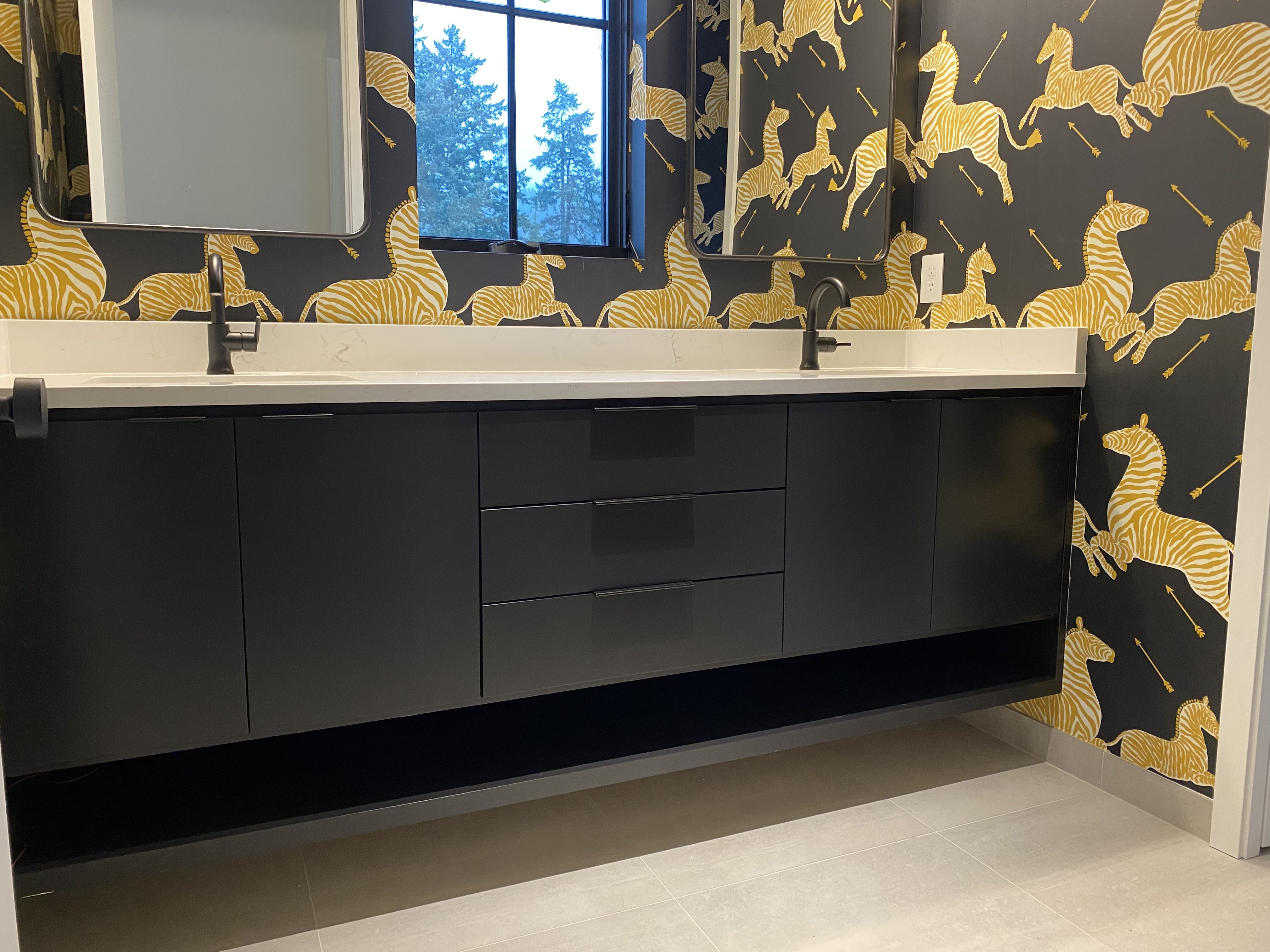Matte black floating double vanity with white quartz countertop and matte black faucets against bold black-and-gold zebra print wallpaper