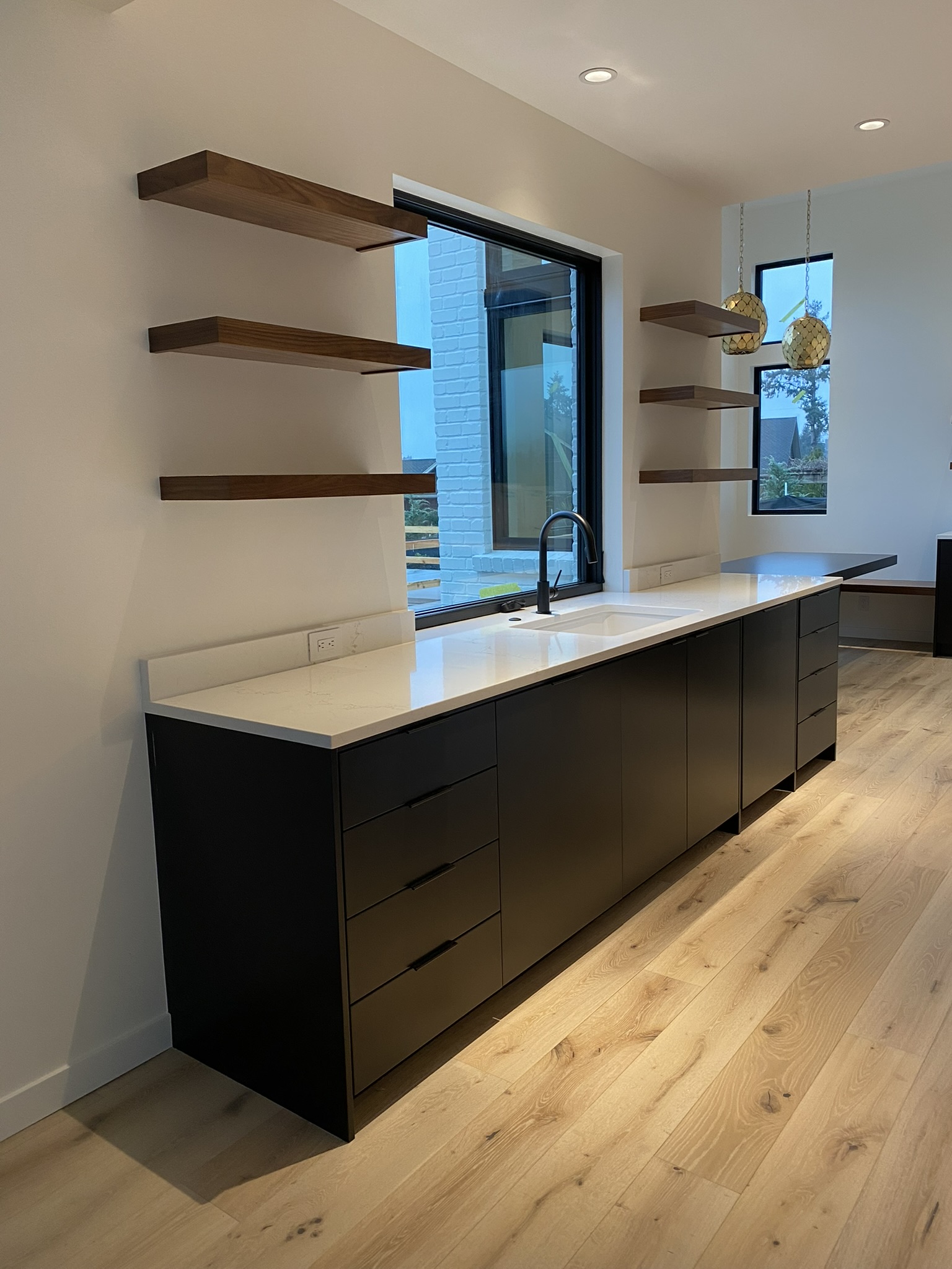 Full kitchen view showing floating walnut shelves, matte black cabinetry, and stone countertops