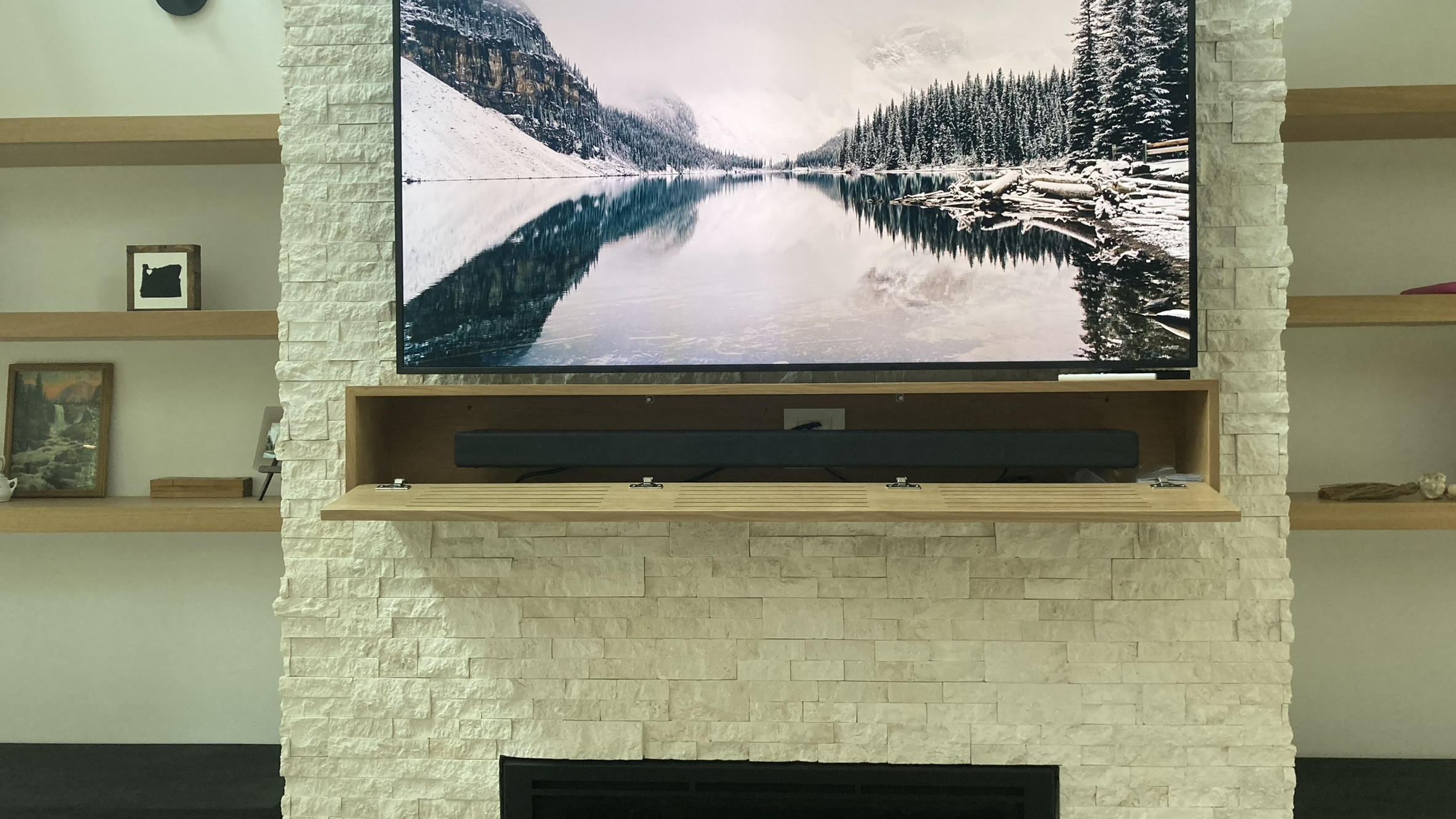 Detail of custom slatted media mantle with integrated soundbar concealment on stone fireplace surround