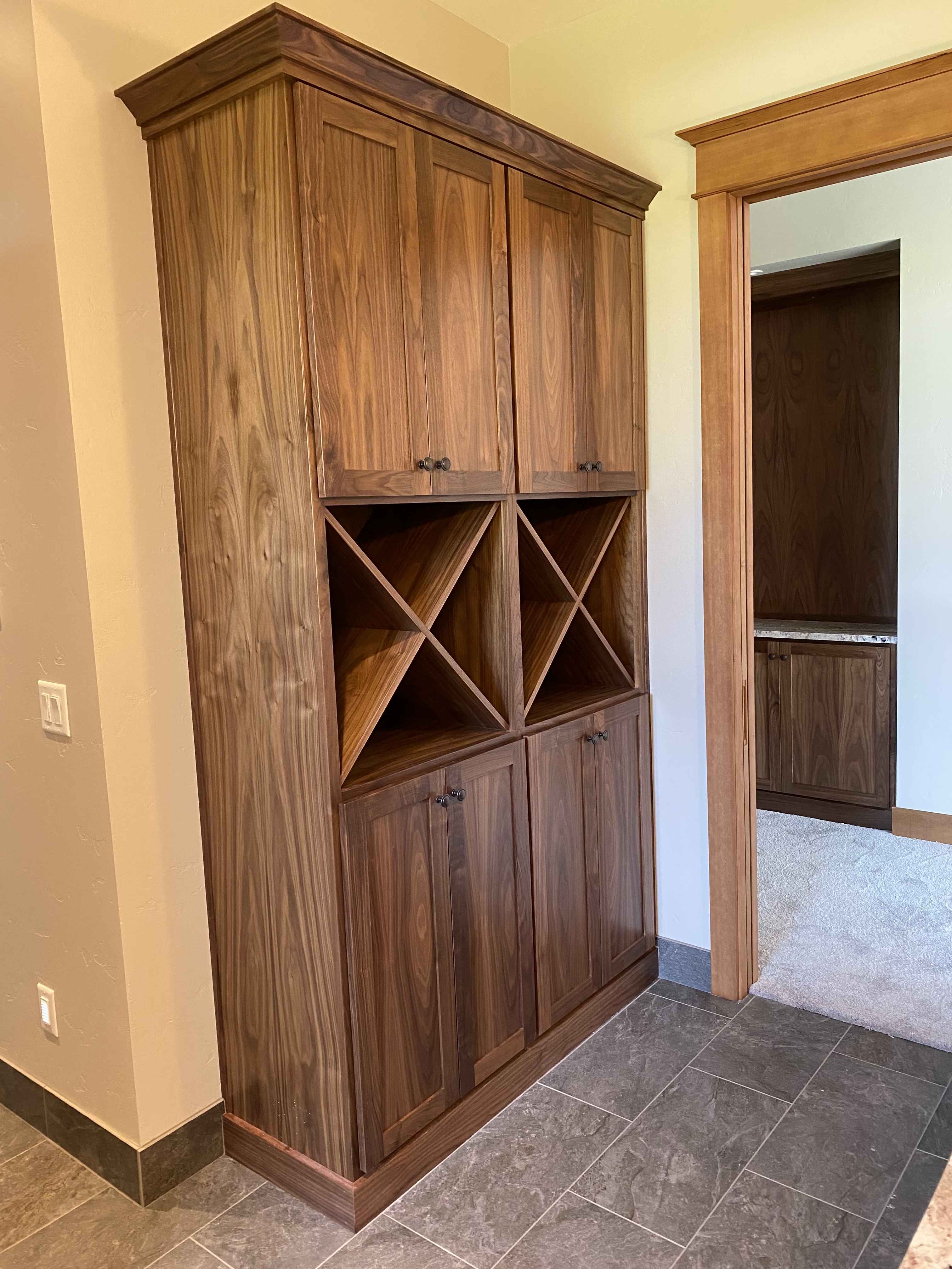 Tall walnut built-in with diamond wine rack center section, upper and lower cabinet doors, and dark hardware