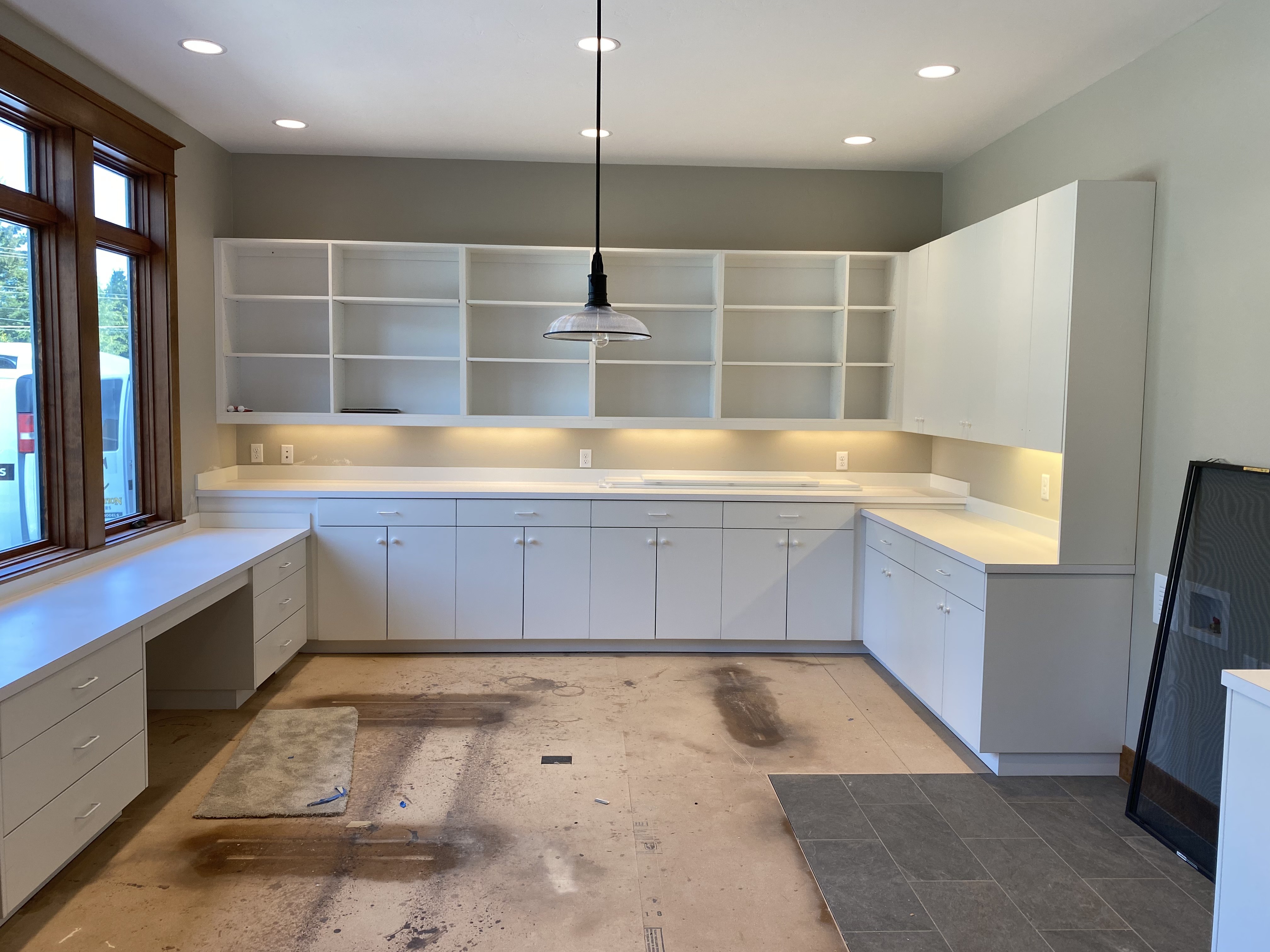 Wide view of a custom white craft room with wraparound base cabinets, floor-to-ceiling open shelving, and window-facing work counter