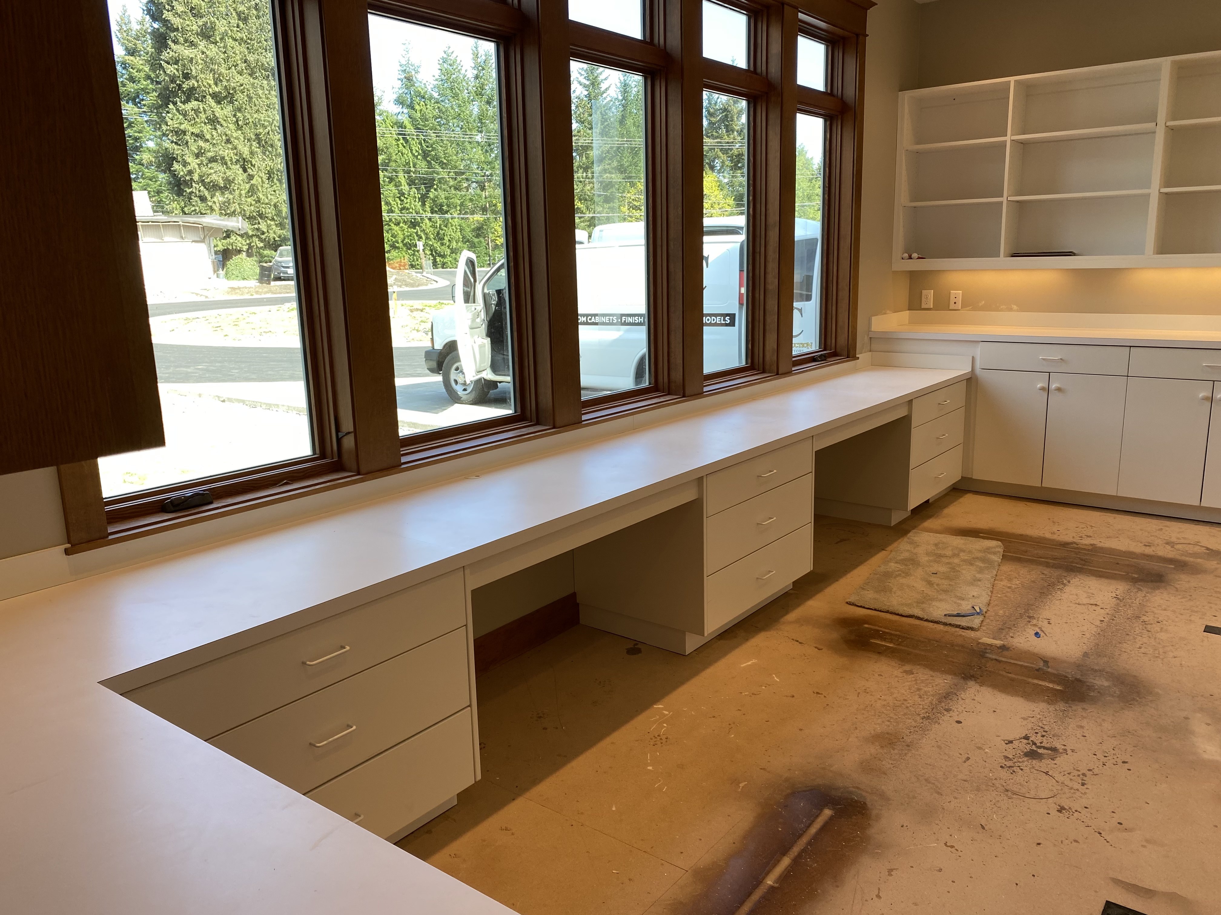 Close-up of the window-facing work counter with drawer pedestals and open shelving above in a custom craft studio