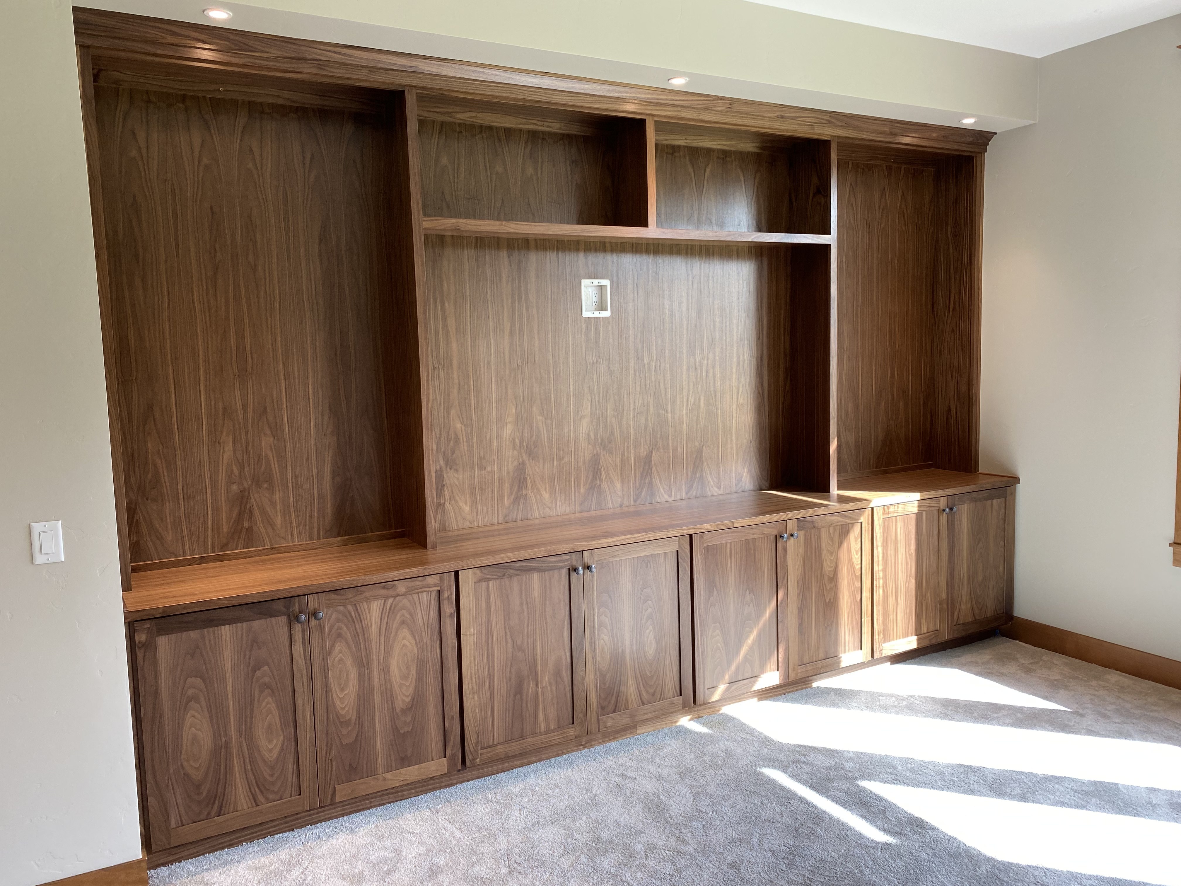 Full-wall walnut media built-in with open shelving above and base cabinets below, integrated lighting