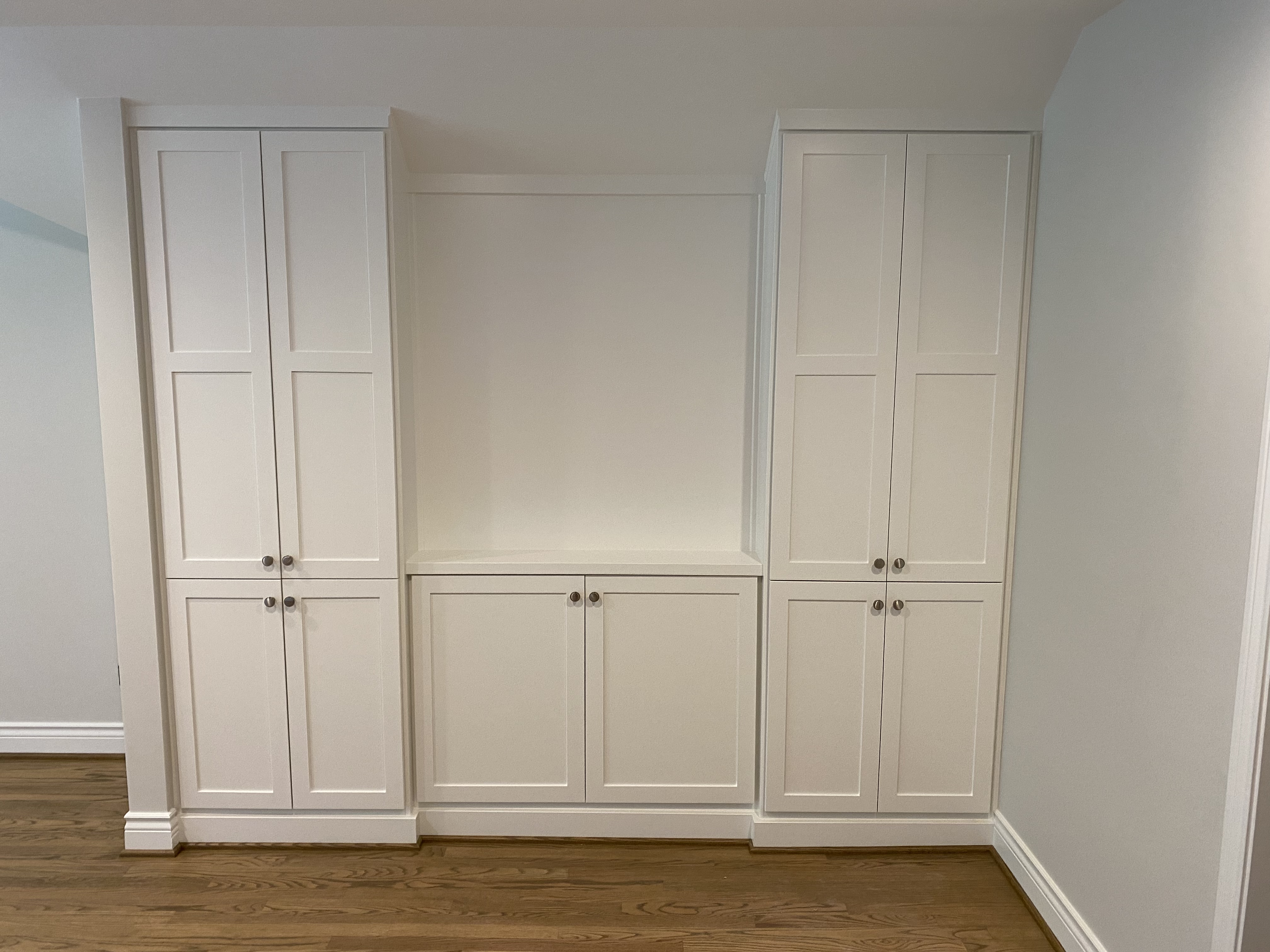 White shaker built-in cabinetry wall — the right panel is a hidden door, seamless from the outside