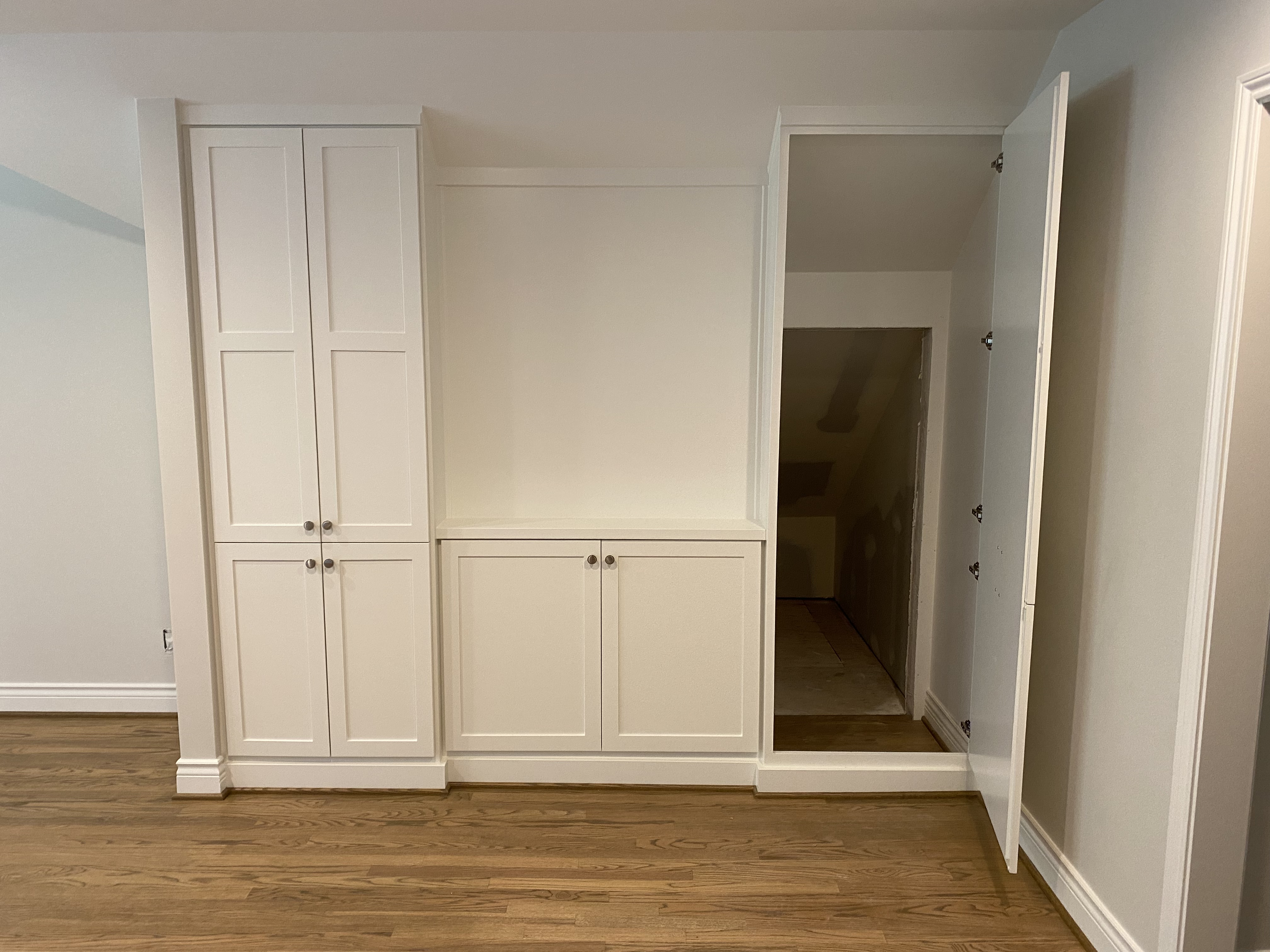 White shaker hidden door swung open, revealing the staircase concealed behind the built-in cabinetry