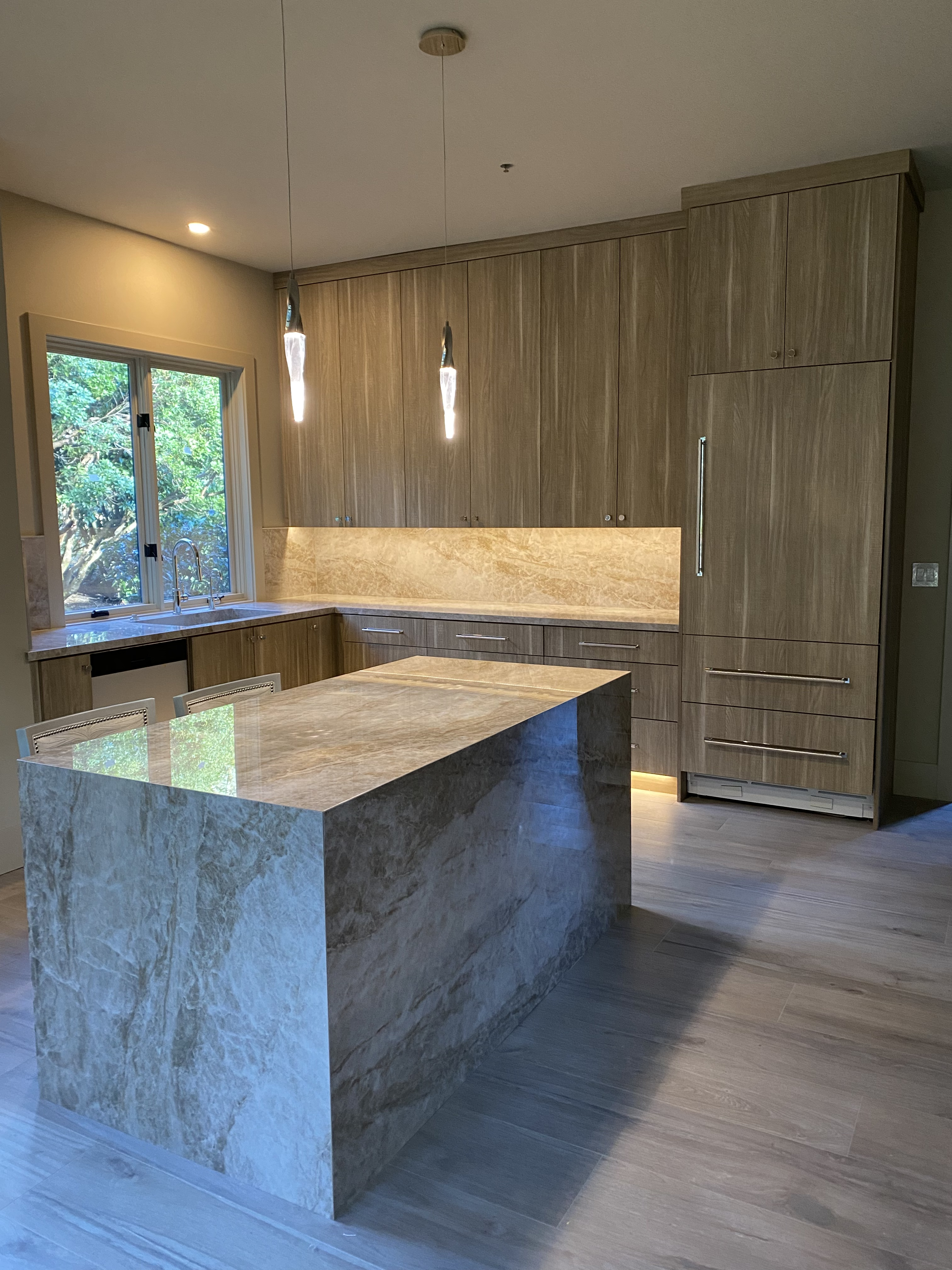 Second view of wood grain kitchen showing full cabinet run, stone backsplash, and large stone island with bar seating