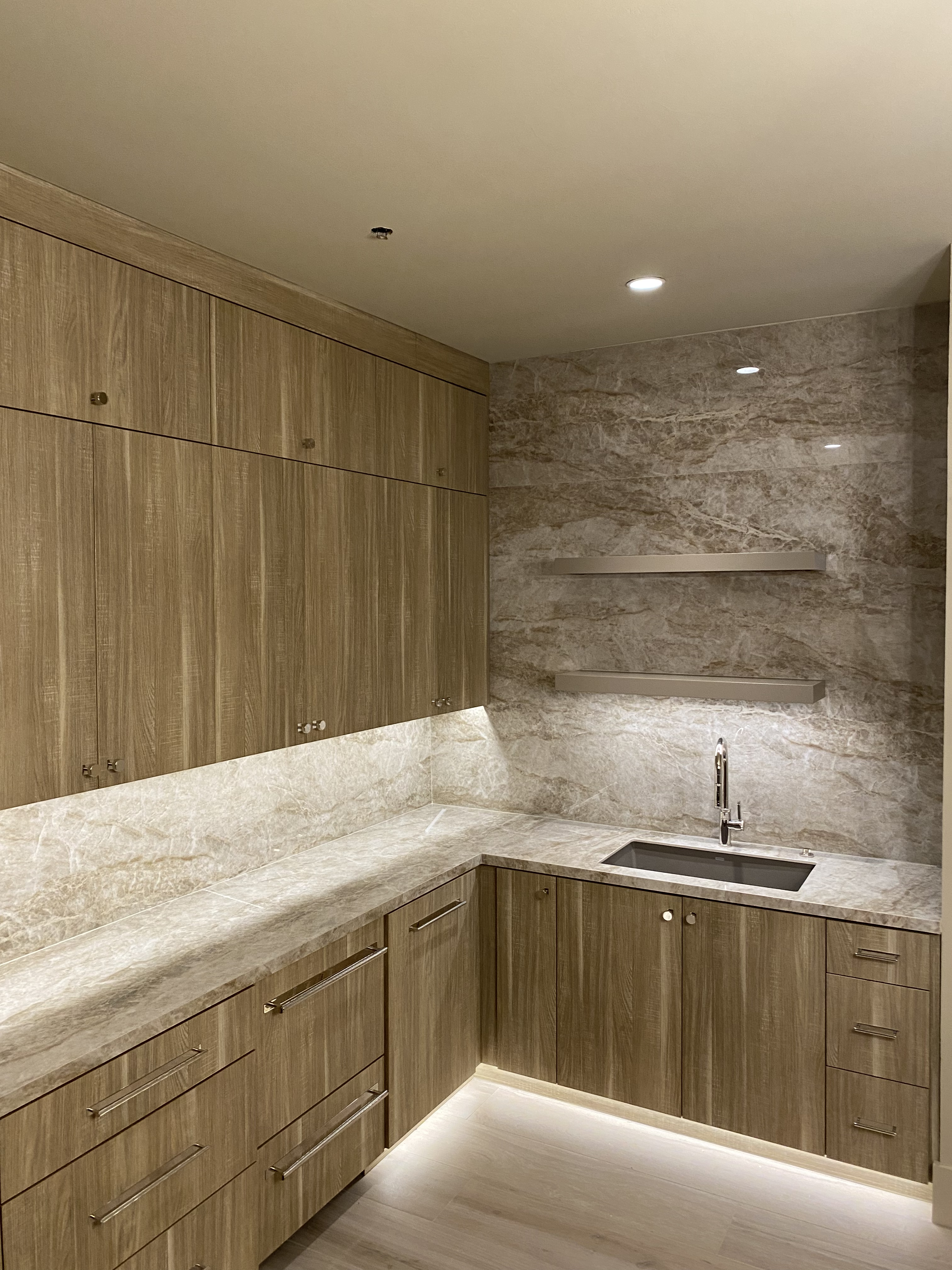 Custom man cave with wood grain floor-to-ceiling cabinetry, stone countertop and backsplash, undermount sink, and LED underlighting