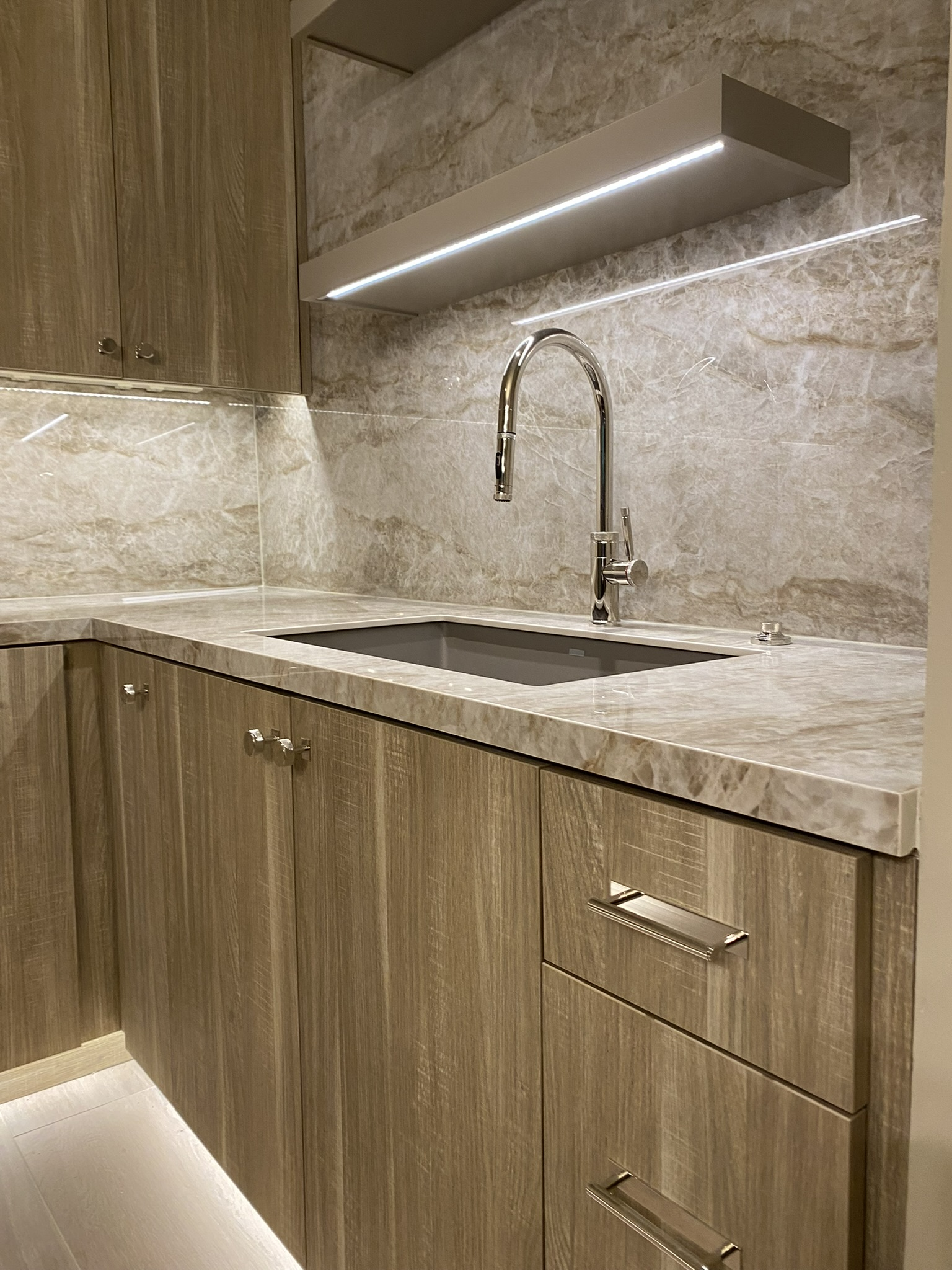 Close-up detail of man cave sink area with wall-mount faucet, stone surround, and wood grain cabinet fronts